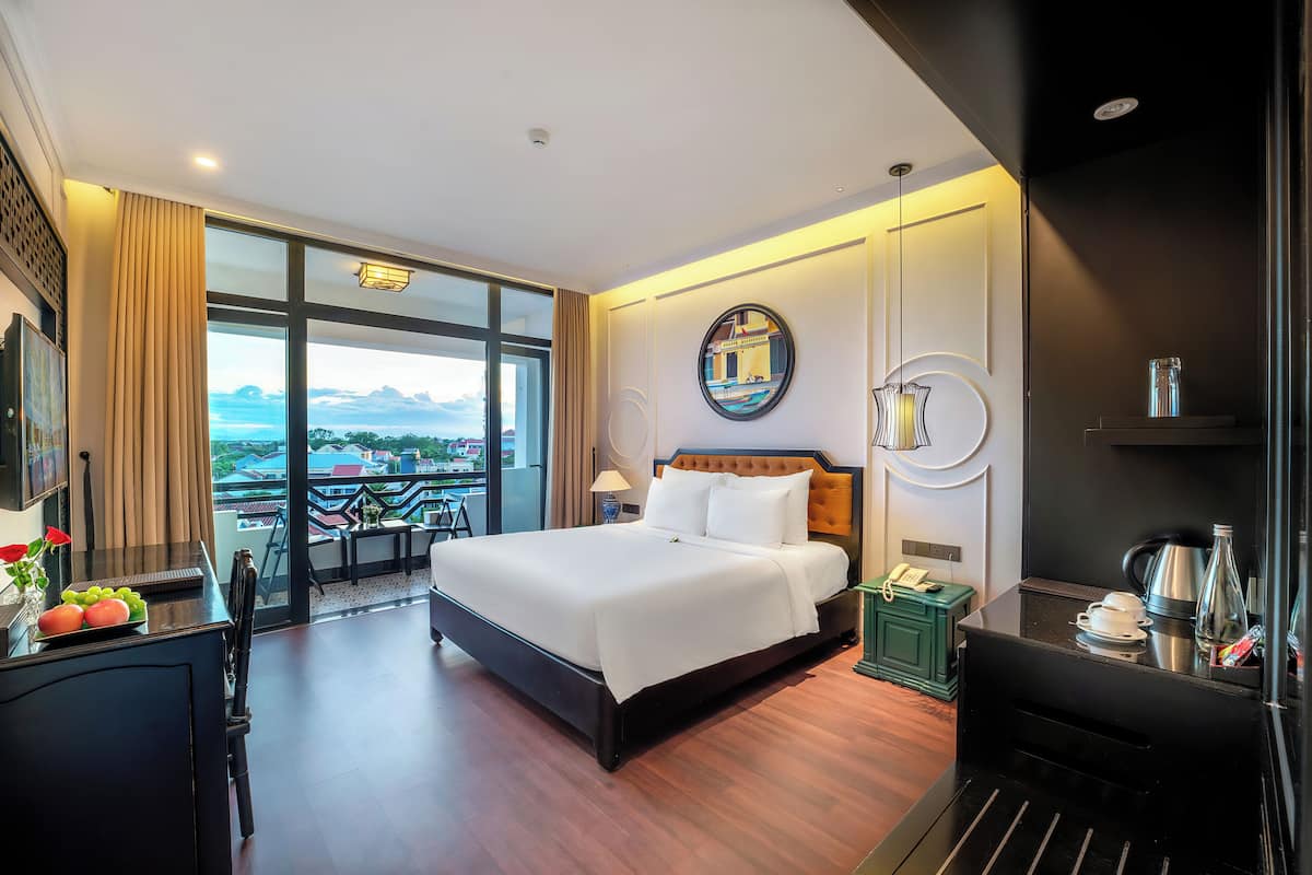 A hotel room with a large bed, a desk with a telephone, a coffee maker, and a view of the cityscape.