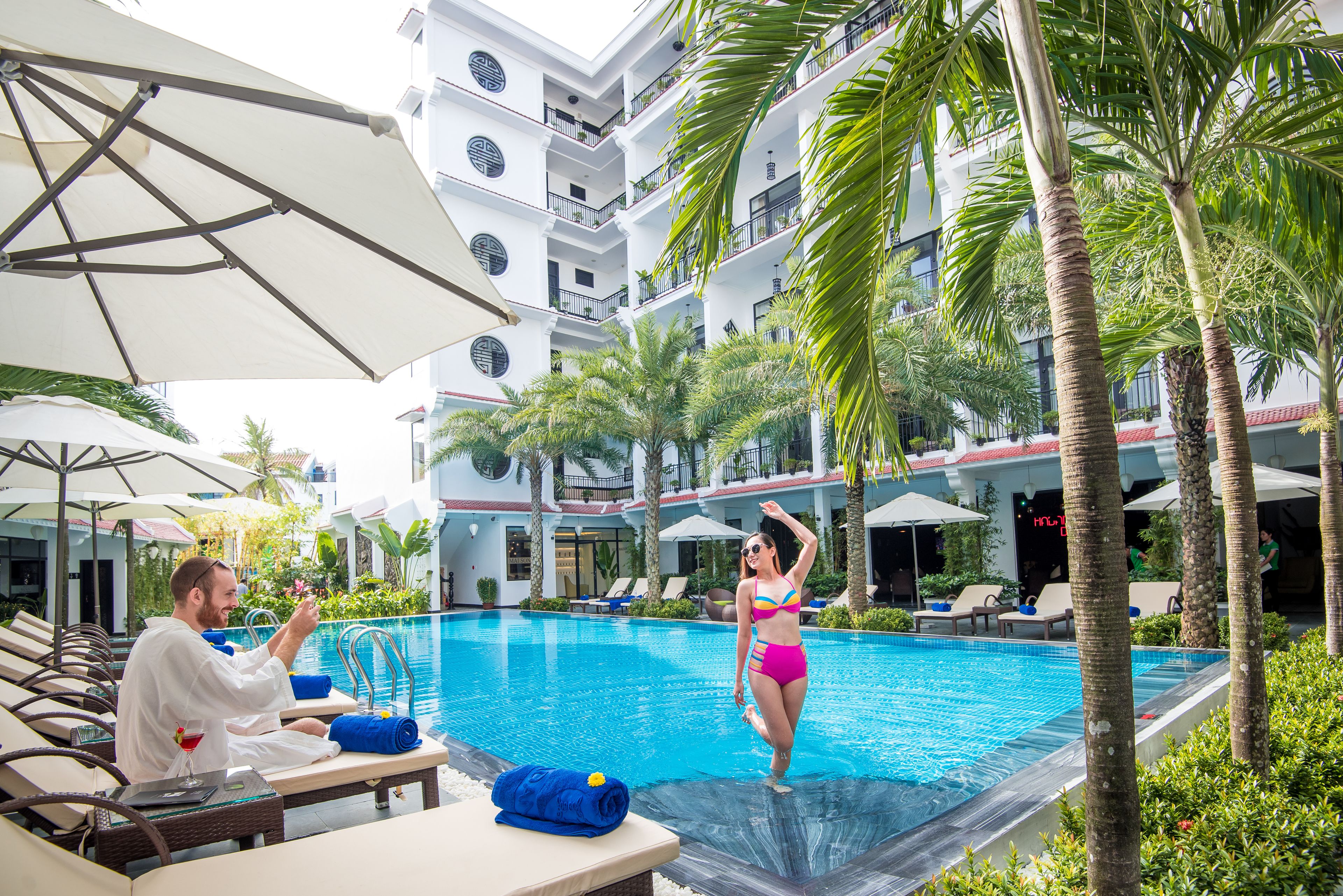 A pool area with lounge chairs, umbrellas, and palm trees.