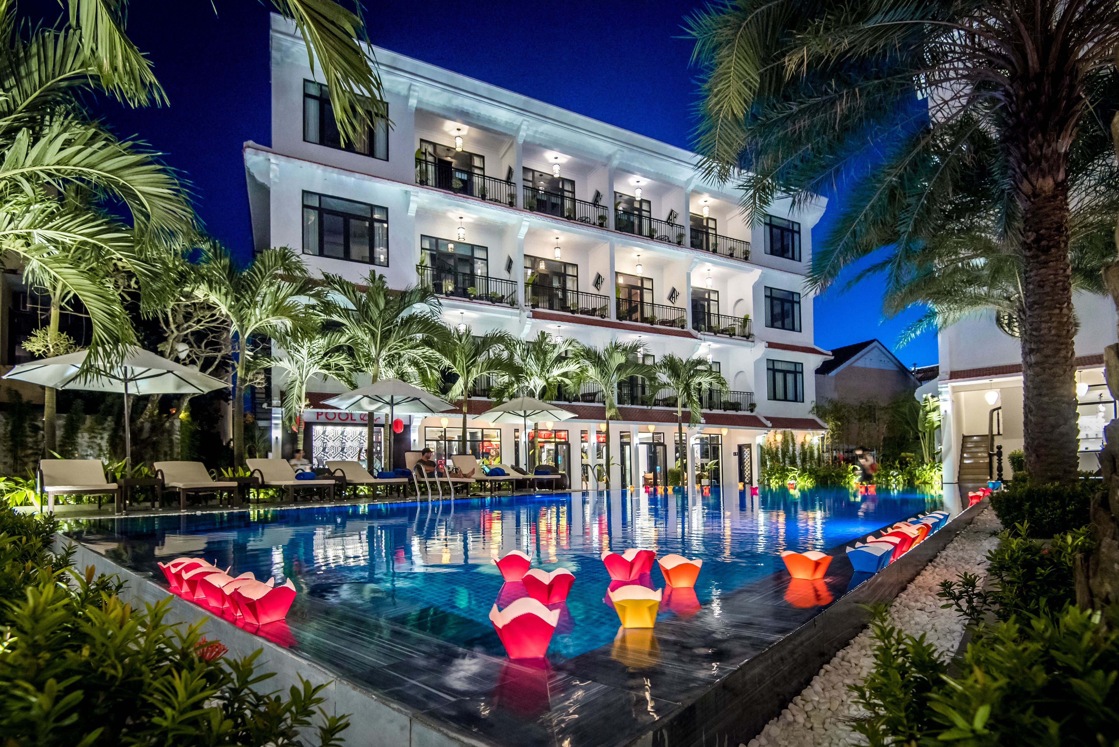 A multi-story hotel with a swimming pool, palm trees, and outdoor seating areas.