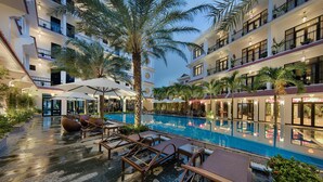 A hotel courtyard with a pool, lounge chairs, and palm trees. - Hadana Boutique Resort Hoi An (Da Nang)