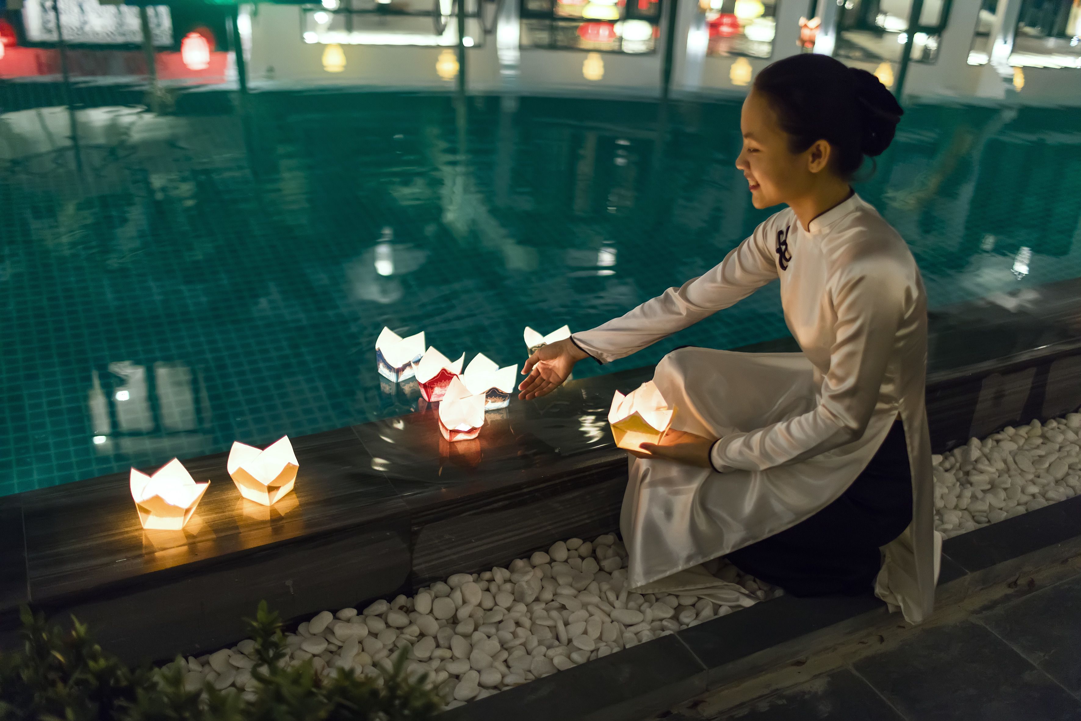 A person sitting by a poolside with paper lanterns.