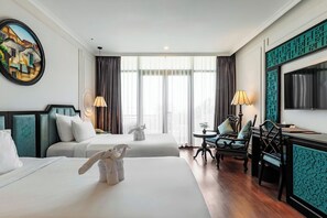 A hotel room with two beds, a desk, a chair, a lamp, and a painting on the wall. - Hadana Boutique Resort Hoi An (Da Nang)