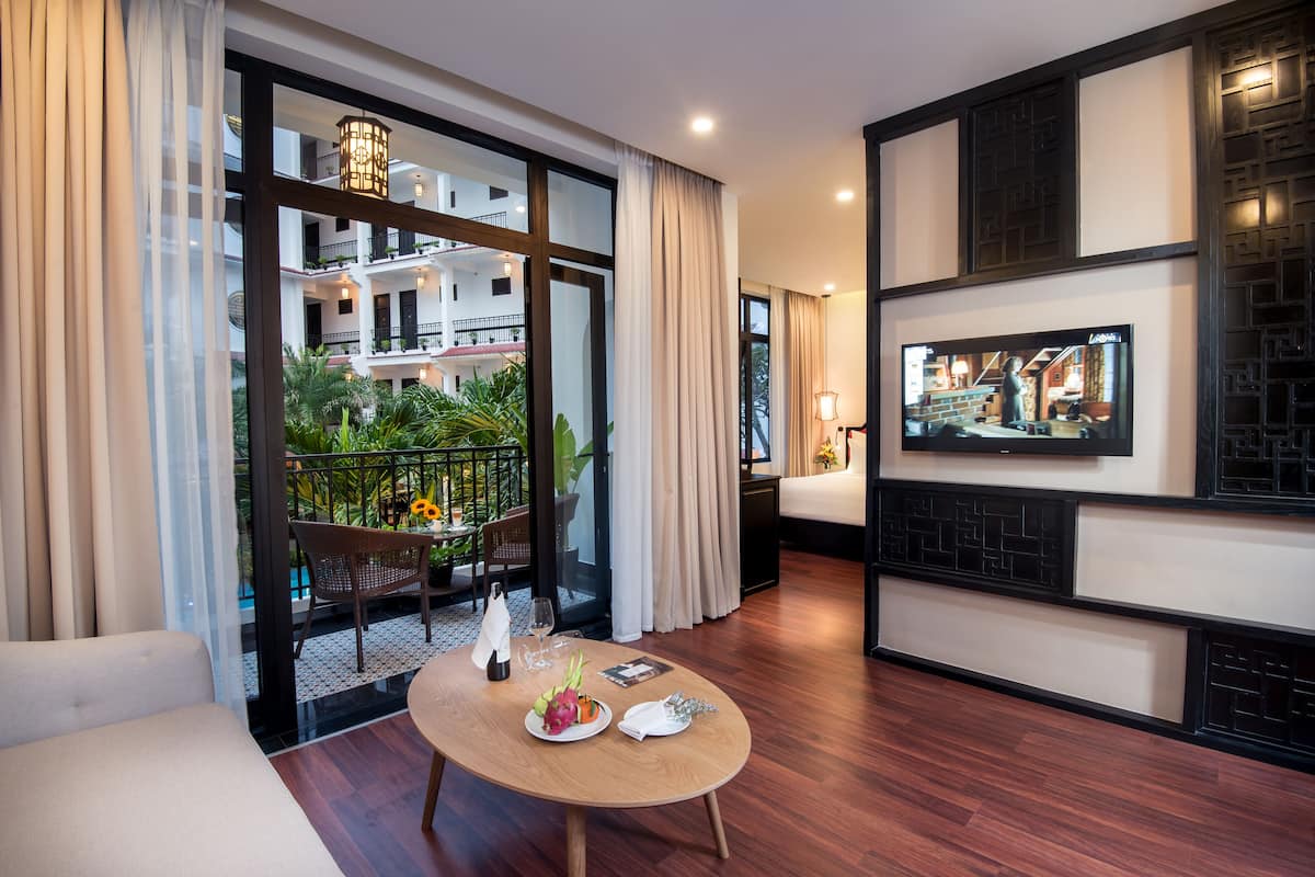 A modern hotel room with a balcony, a dining table with a plate of fruit, and a television mounted on the wall.