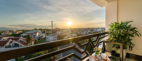 Un balcón con vistas a un paisaje urbano al atardecer, una mesa con una planta y una silla.