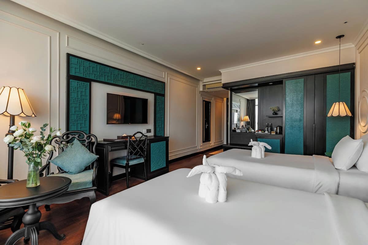A hotel room with a bed, a desk, a chair, a TV, and a bathroom mirror.