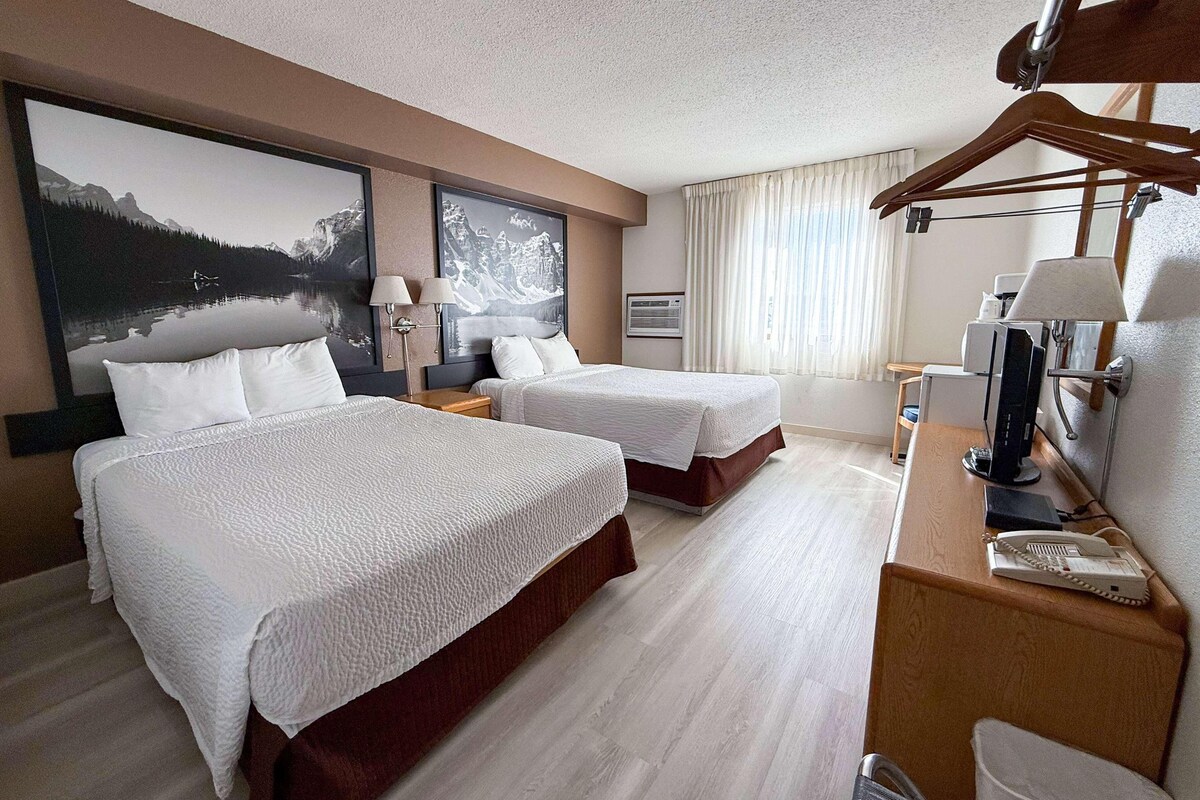 A hotel room with two beds, a desk with a computer, a telephone, and a mirror.