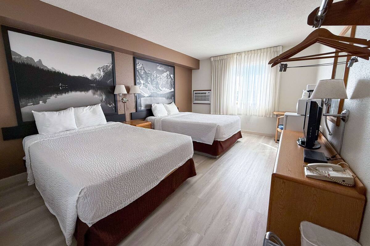 Ett hotellrum med två sängar, ett skrivbord med en dator, en telefon och en spegel.