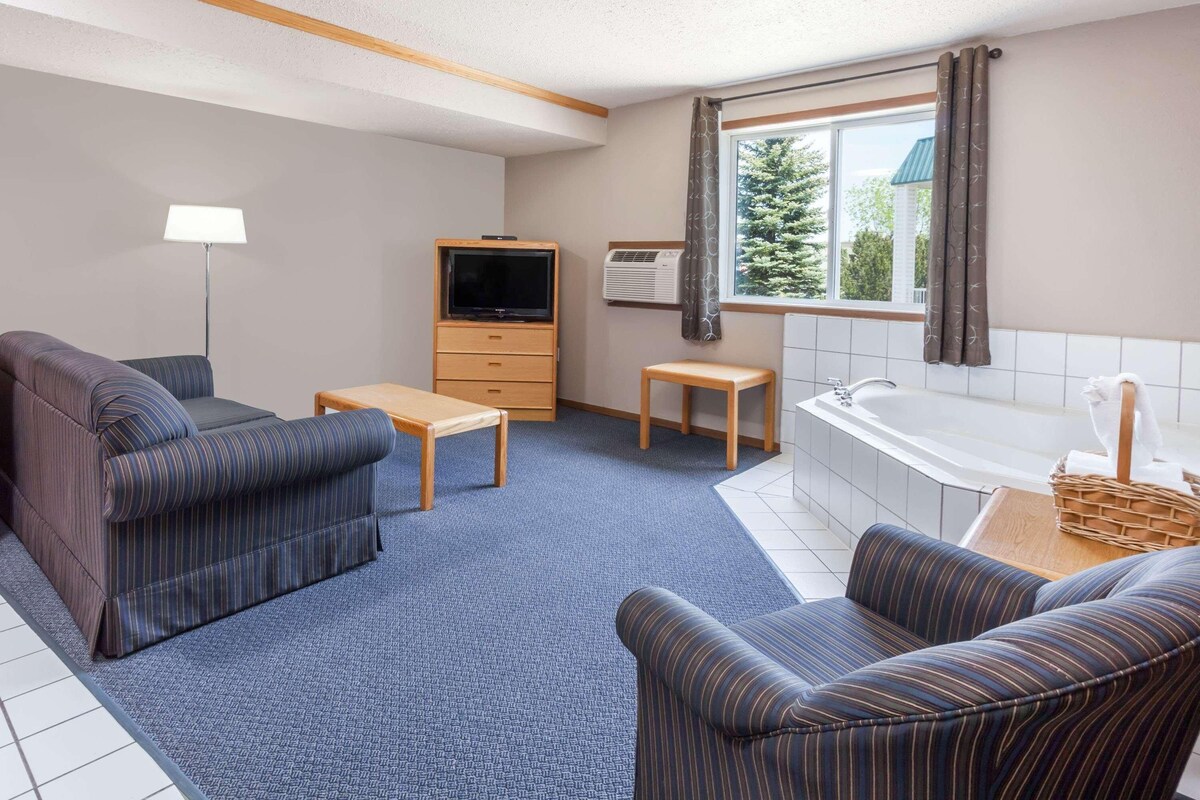 A room with a sofa, a television, a small table, a bench, a bathtub, and a window with curtains.