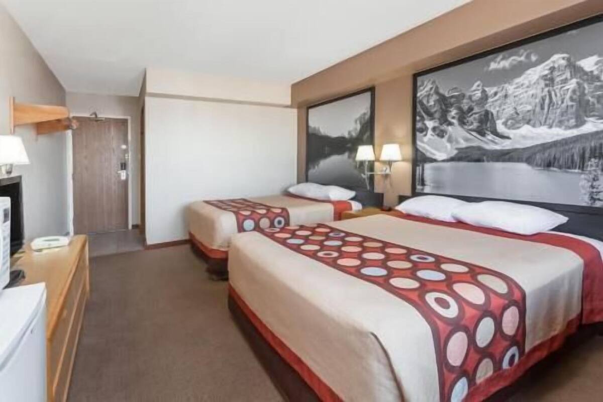 Ett hotellrum med två sängar, ett skrivbord, en stol och ett stort fönster med utsikt över bergen.