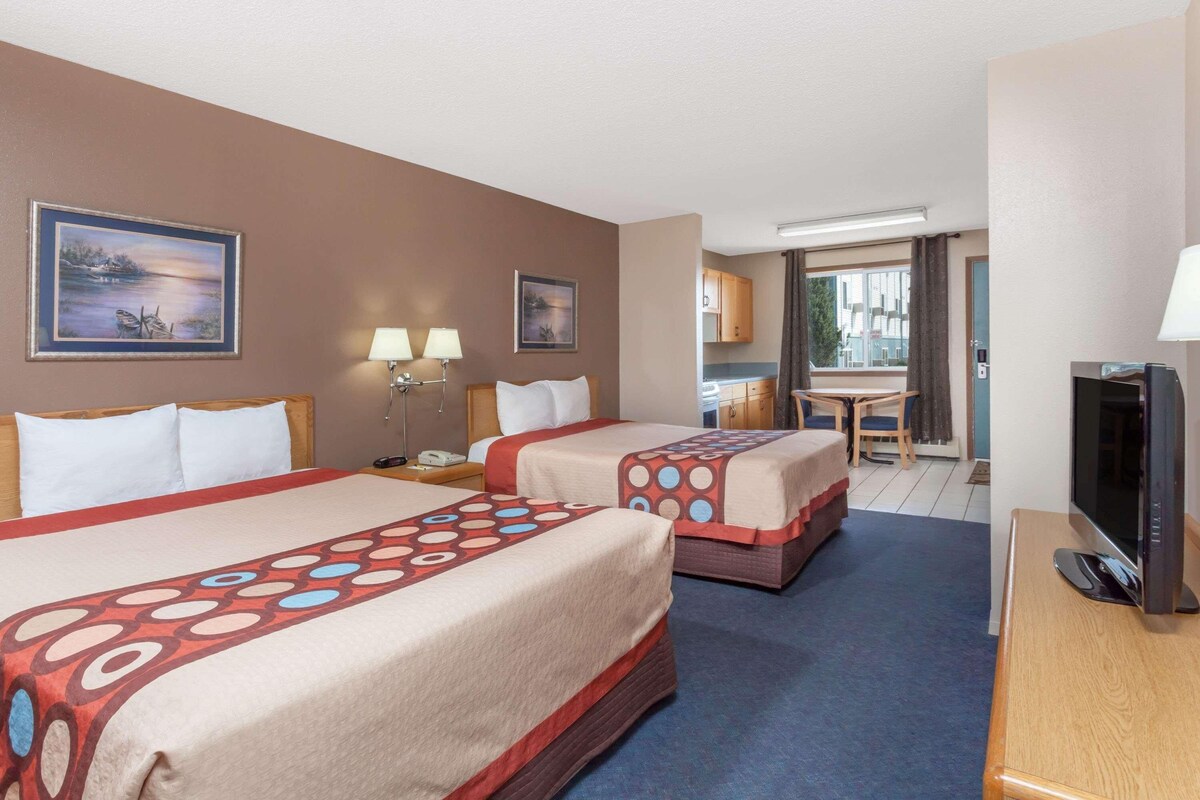 A hotel room with two beds, a television, a desk, and a kitchenette.