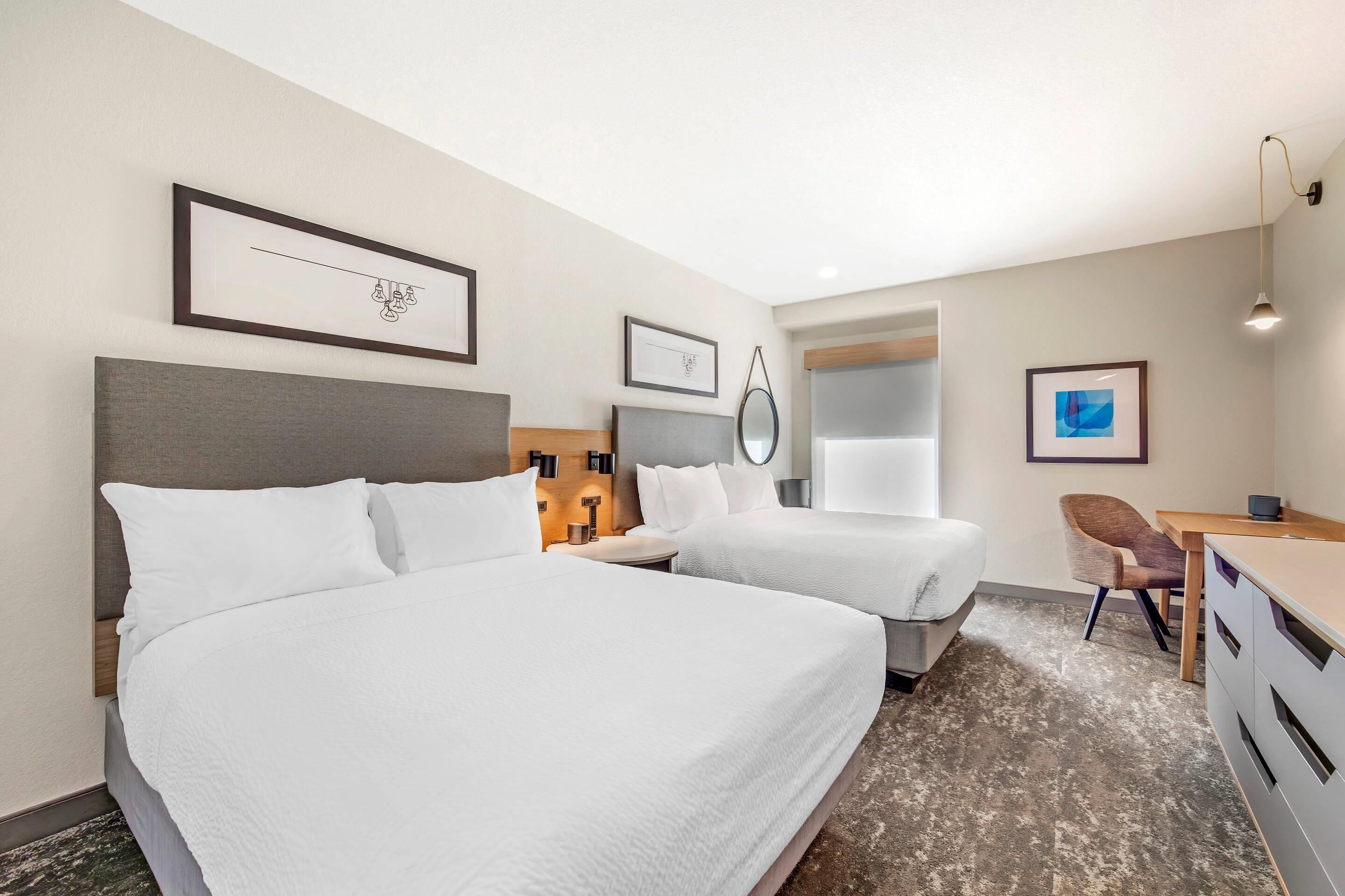 A hotel room with two beds, a desk, a chair, and a small table.