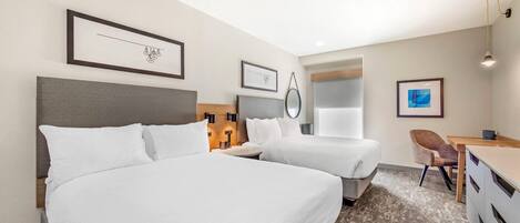 A hotel room with two beds, a desk, a chair, and a small table.