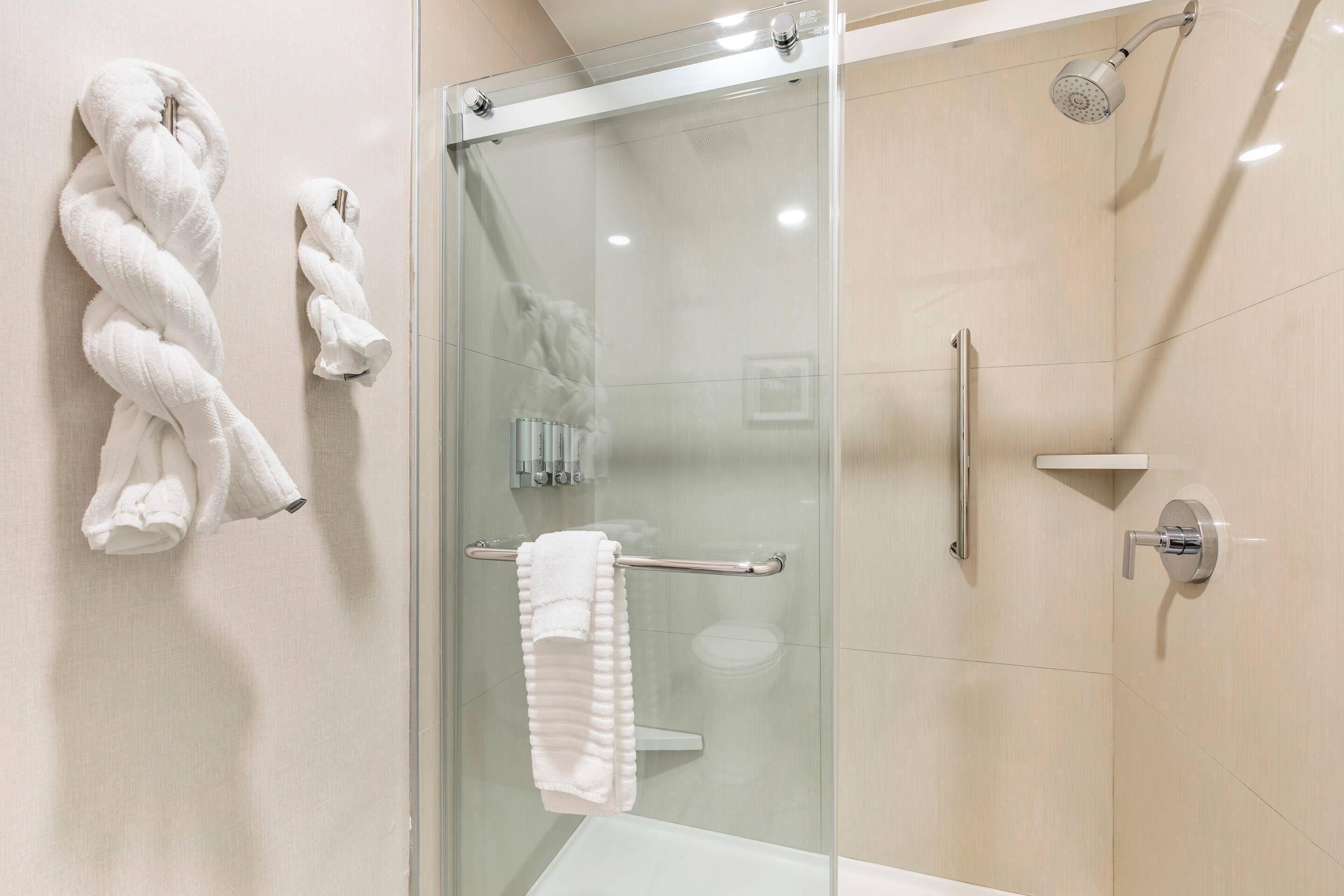 A modern bathroom with a glass shower enclosure, a white bathtub, and two towels on the wall.