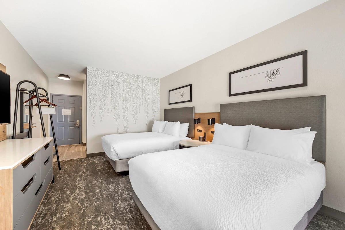 A hotel room with two beds, a desk, a wardrobe, and a bathroom door.