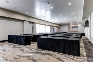 Un salón de conferencias con varias mesas, piso alfombrado e iluminación empotrada en el techo.