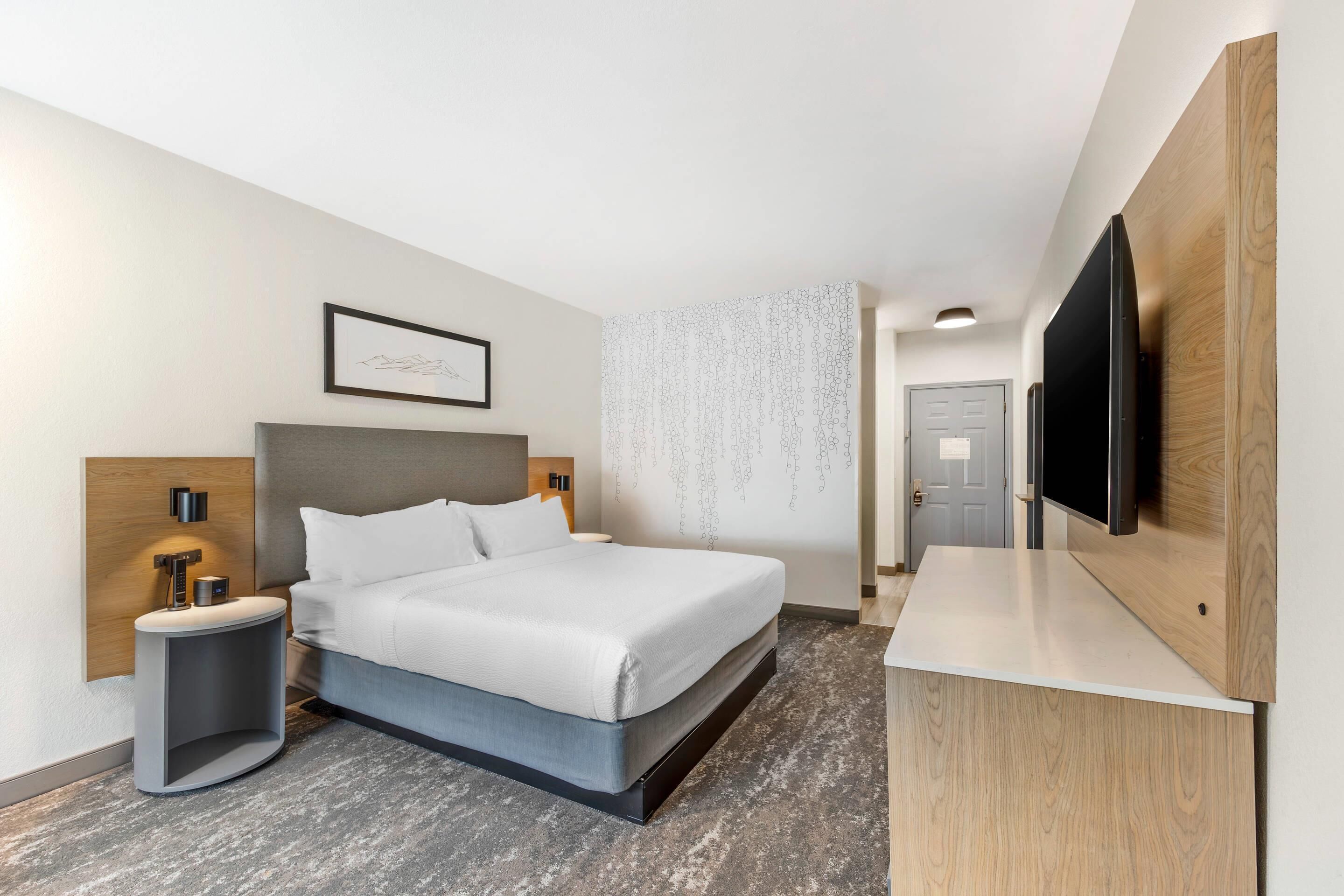 Ein modernes Hotelzimmer mit einem großen Bett, Nachttischen, einem Flachbildfernseher und einer Wand mit Holzapplikationen.
