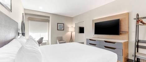 Ein modernes Hotelzimmer mit einem großen Bett, einem Flachbildfernseher an einer Holzvertäfelung, einem Schreibtisch mit Schubladen, einem Stuhl und einer Lampe.