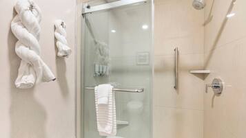 Un baño moderno con mampara de vidrio, una bañera blanca y dos toallas colgadas en la pared.