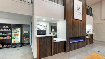 Zona de recepción con un mostrador de madera, una pantalla digital y un refrigerador para bebidas.