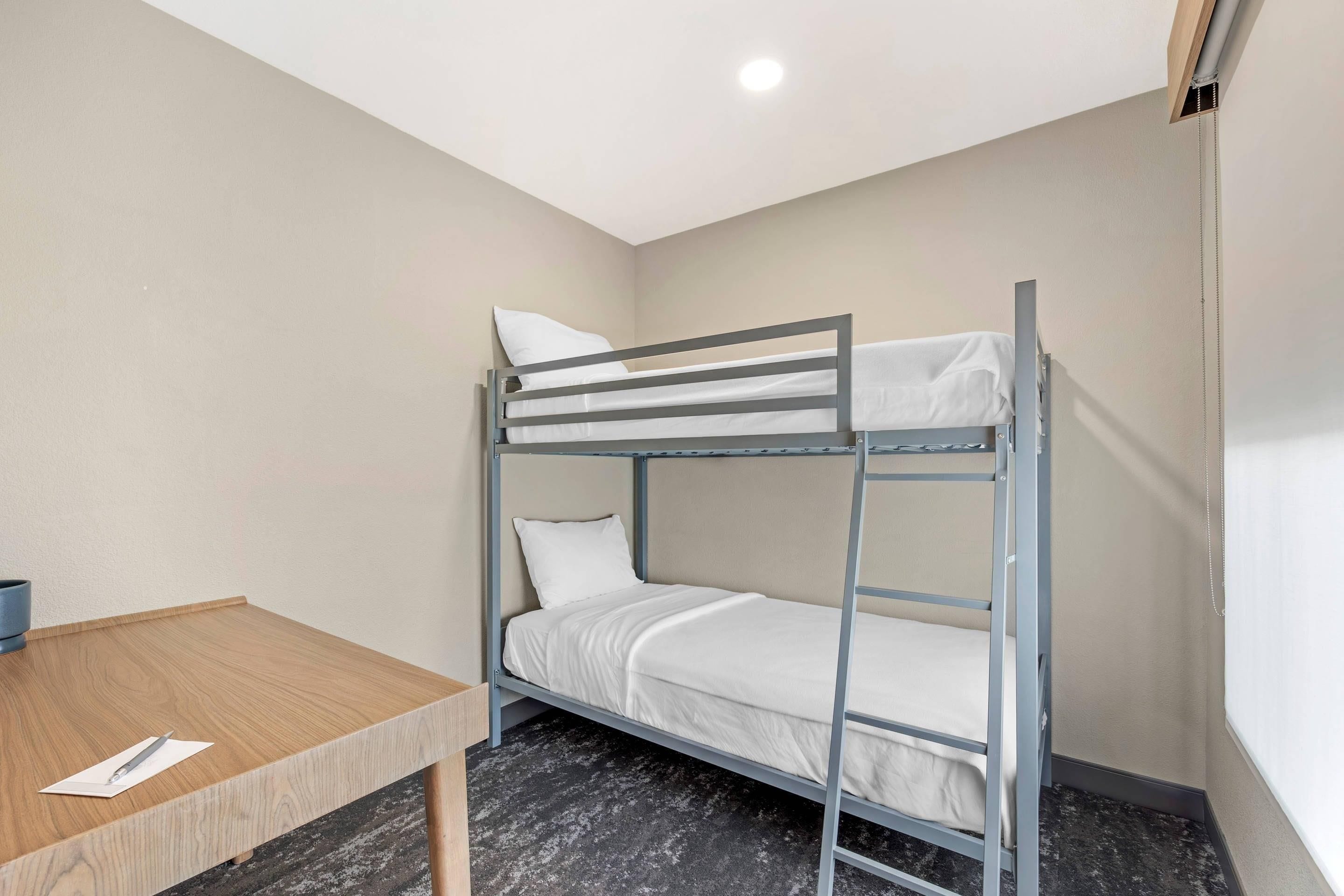 A bunk bed with a wooden table beside it, a white pillow, and a white sheet.