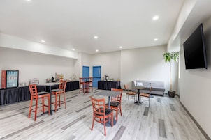 Una sala de conferencias moderna con una mesa larga, varias sillas, un sofá, un televisor y una planta.