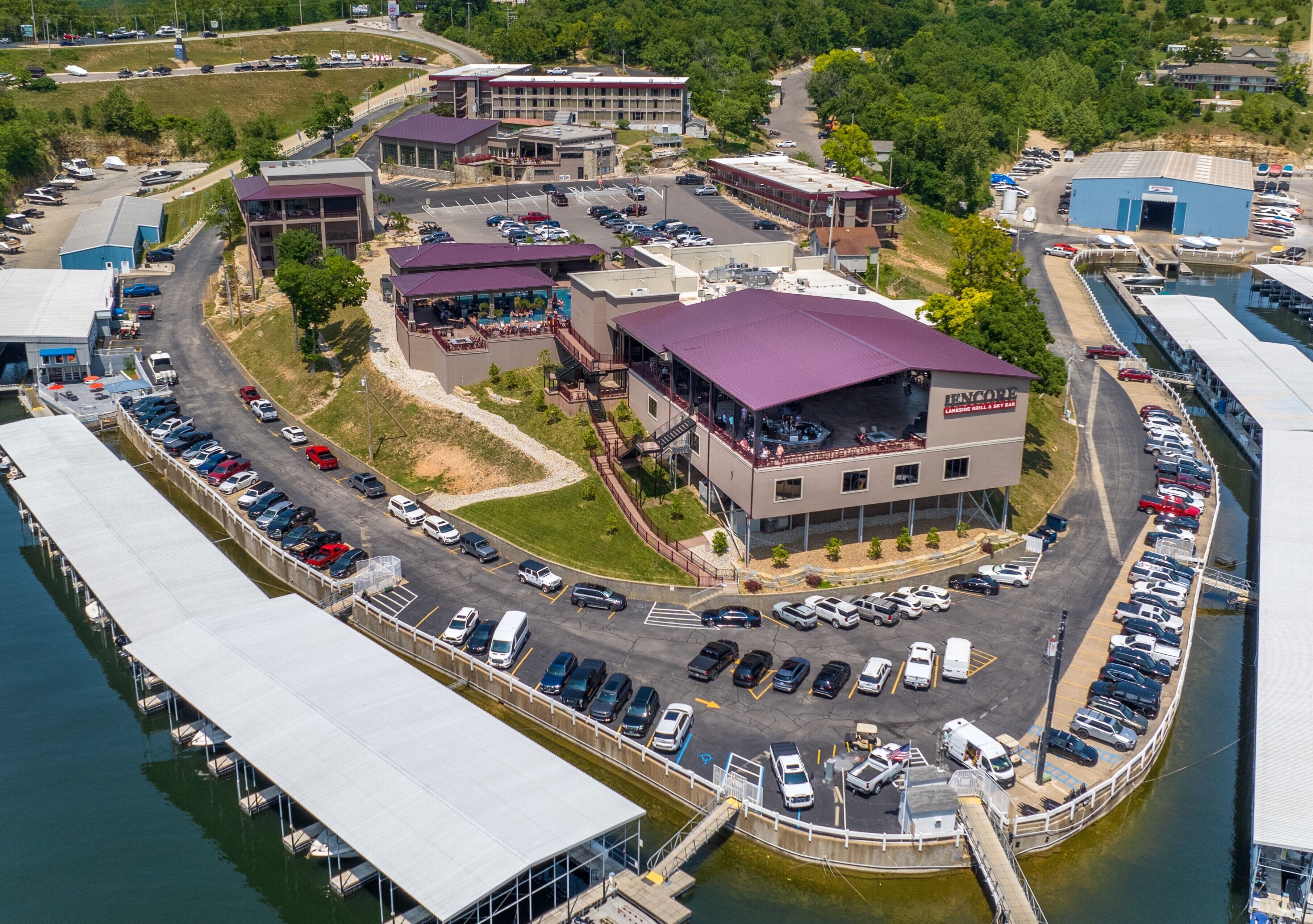 An aerial view of a marina with docked boats, a parking lot, and buildings with purple roofs.