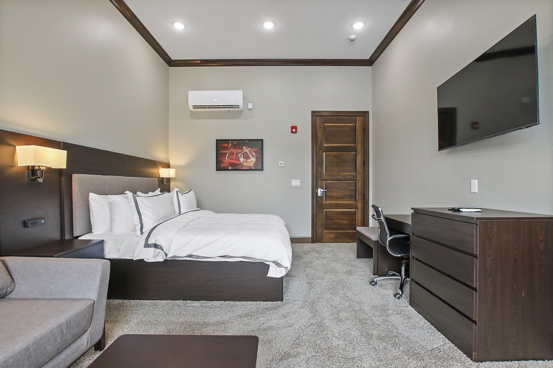 A hotel room with a bed, bedside lamps, a flat-screen TV, a dresser, a desk, and a chair.