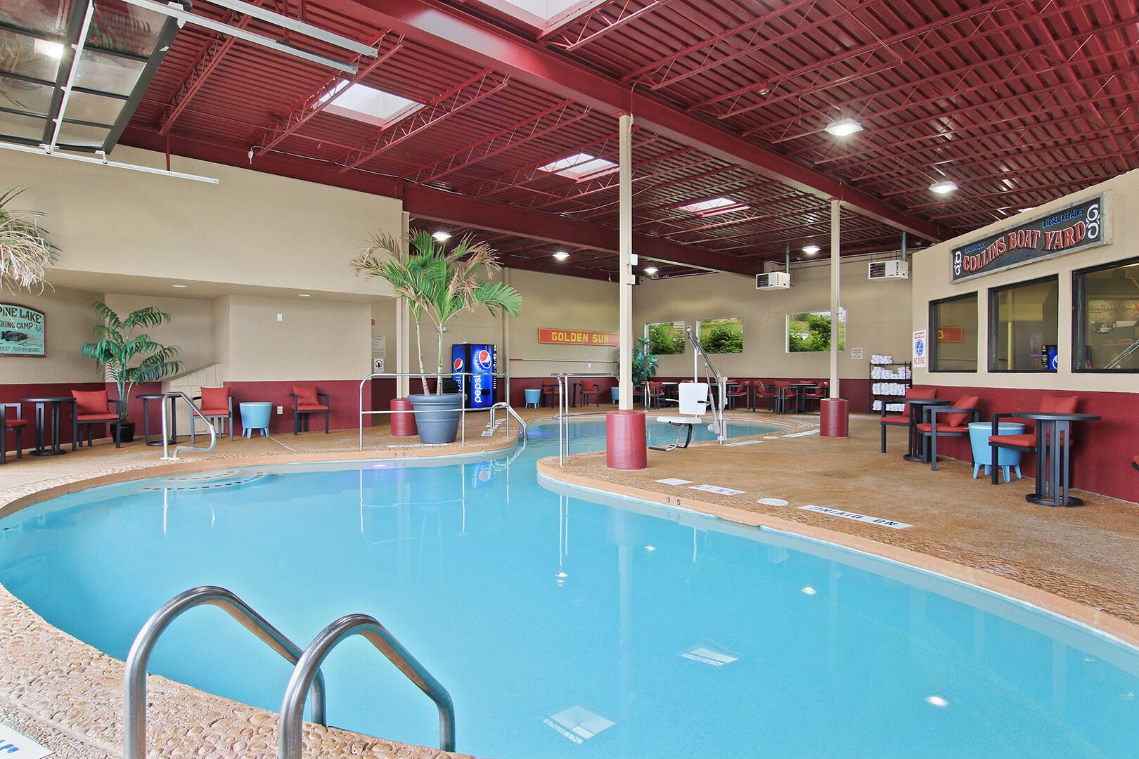 An indoor swimming pool with a red ceiling, seating areas, and a sign for Collins Boat Yard.