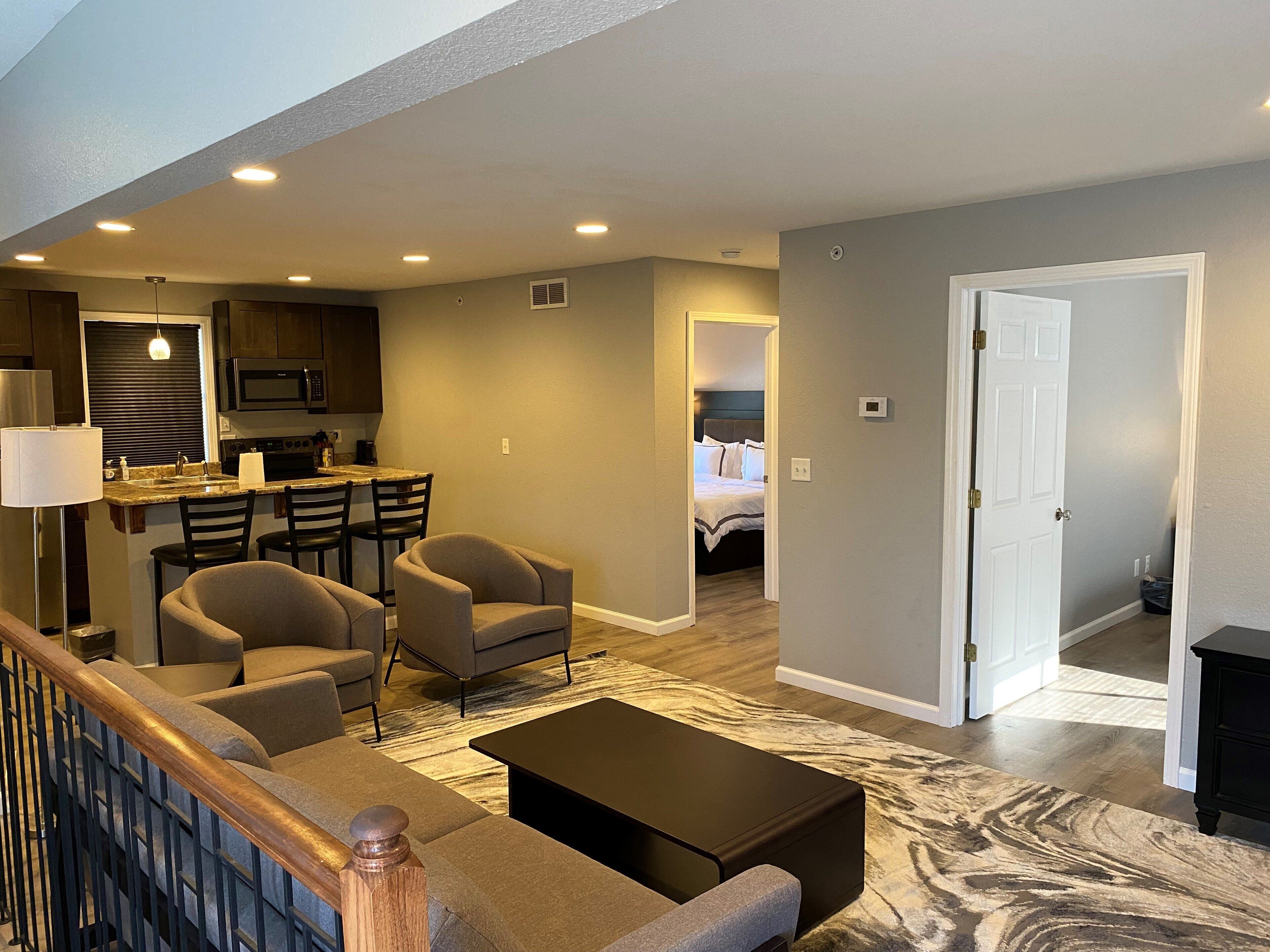 A modern living room with a sofa, chairs, a coffee table, and a kitchen area with a microwave and stove.