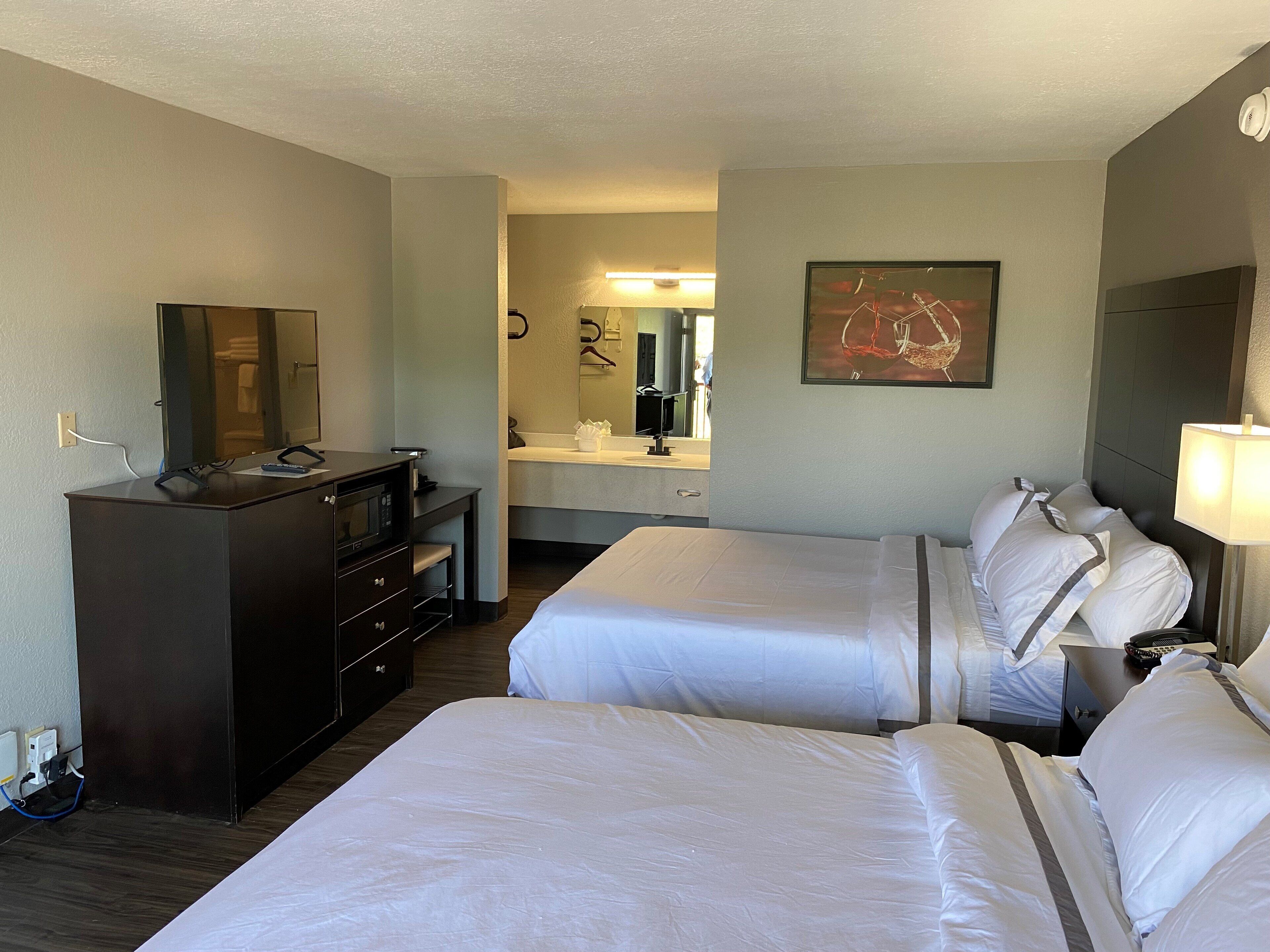 Een hotelkamer met twee bedden, een bureau met spiegel, een dressoir, een badkamer met wastafel en spiegel, en een schilderij aan de muur.
