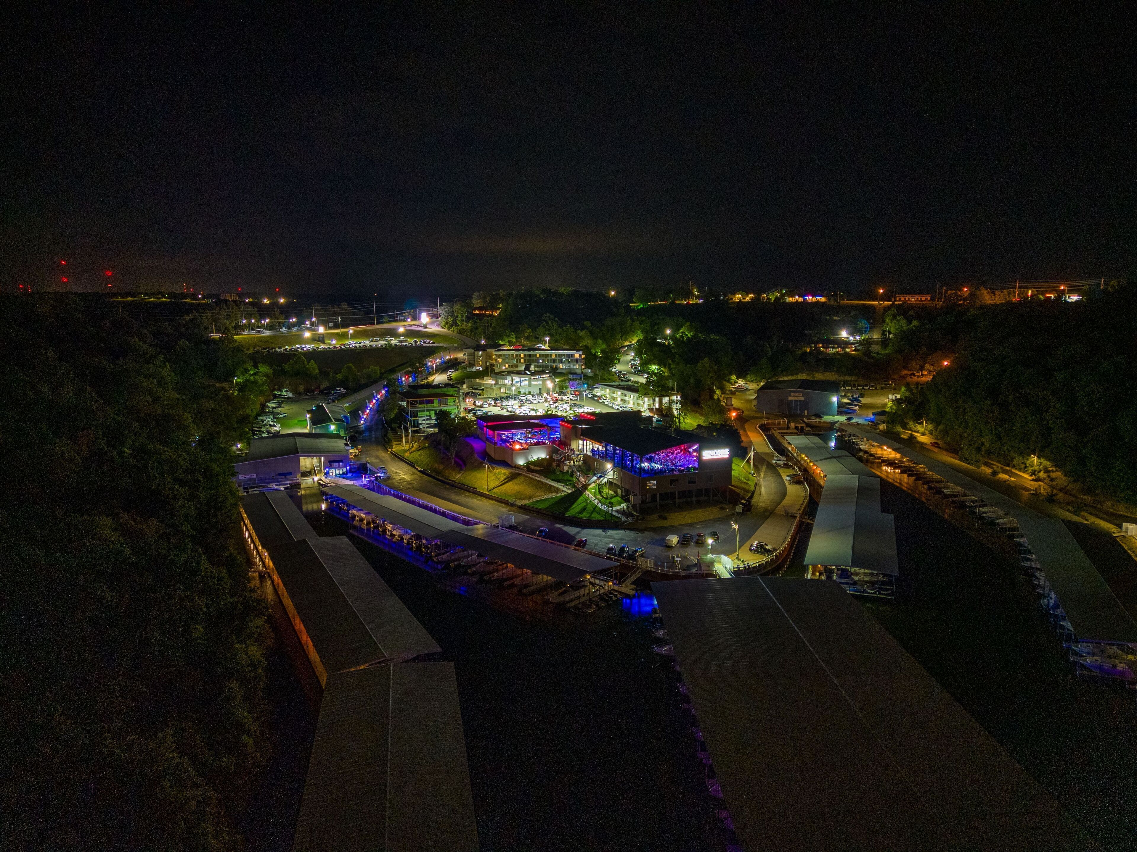 An aerial view of a brightly lit complex with multiple buildings, parking areas, and a road.