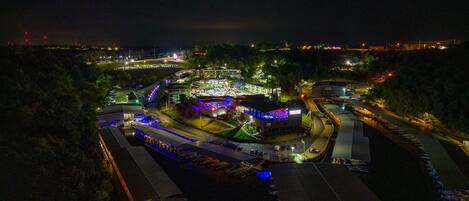 An aerial view of a brightly lit complex with multiple buildings, parking areas, and a road.