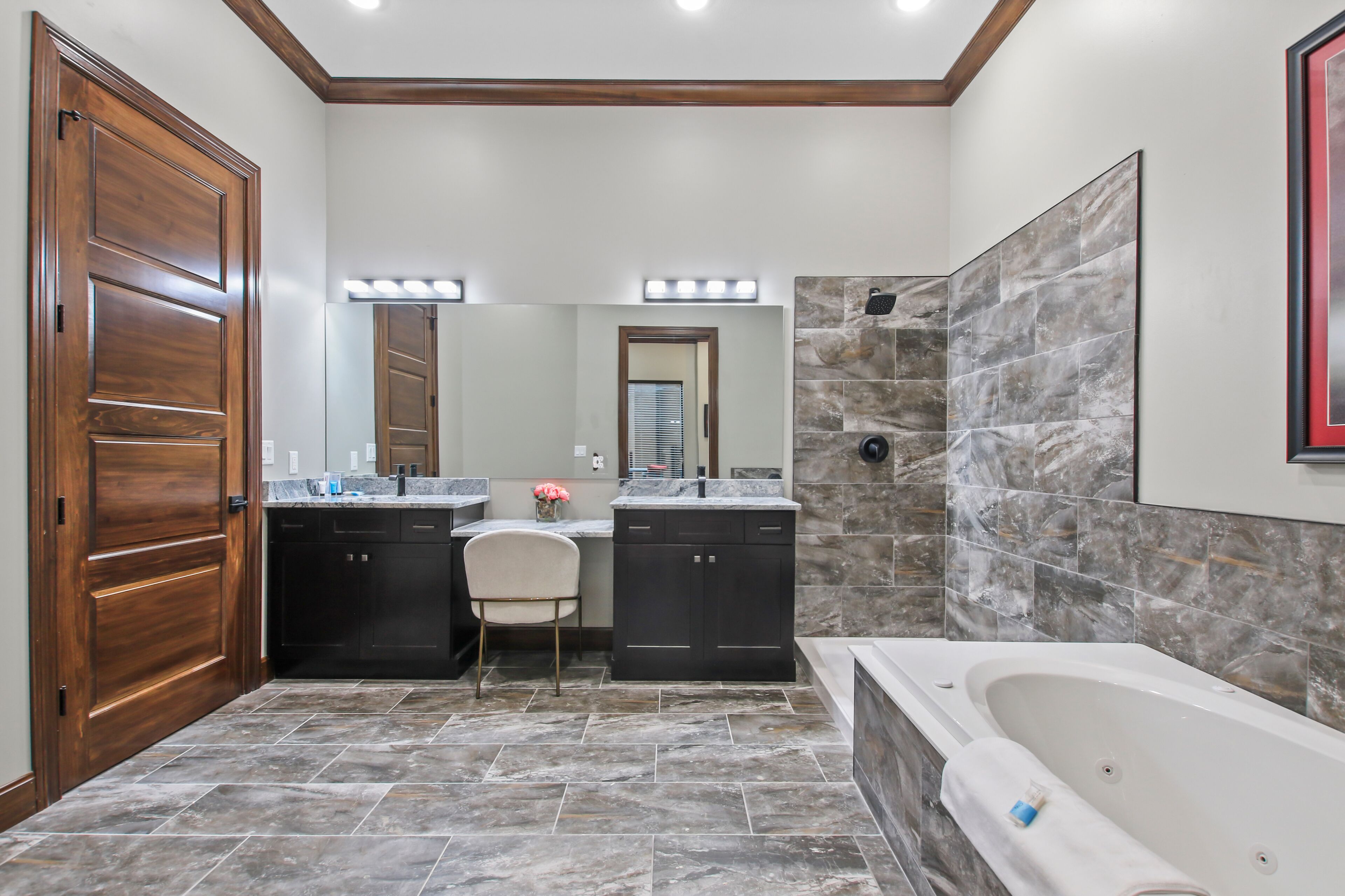 Un baño con puerta de madera, tocador con espejo, lavamanos, una silla y bañera.