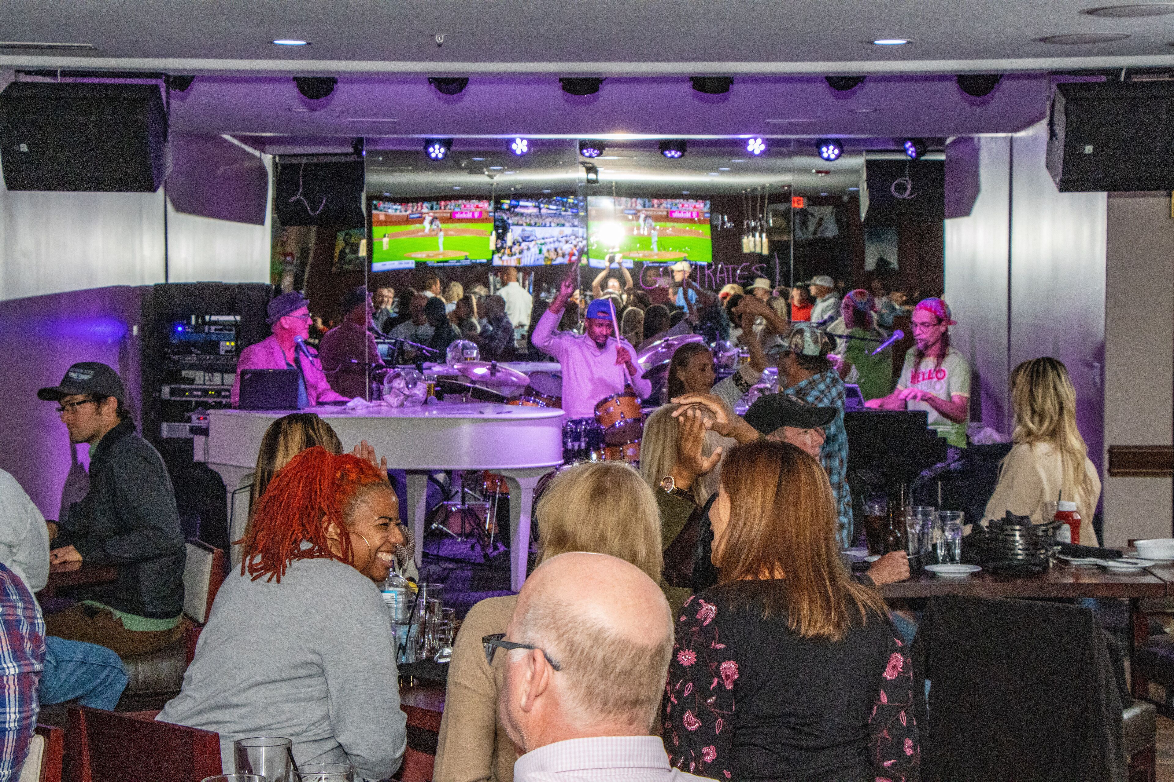 A bar area with multiple screens displaying sports events, a bar counter, and seated patrons.