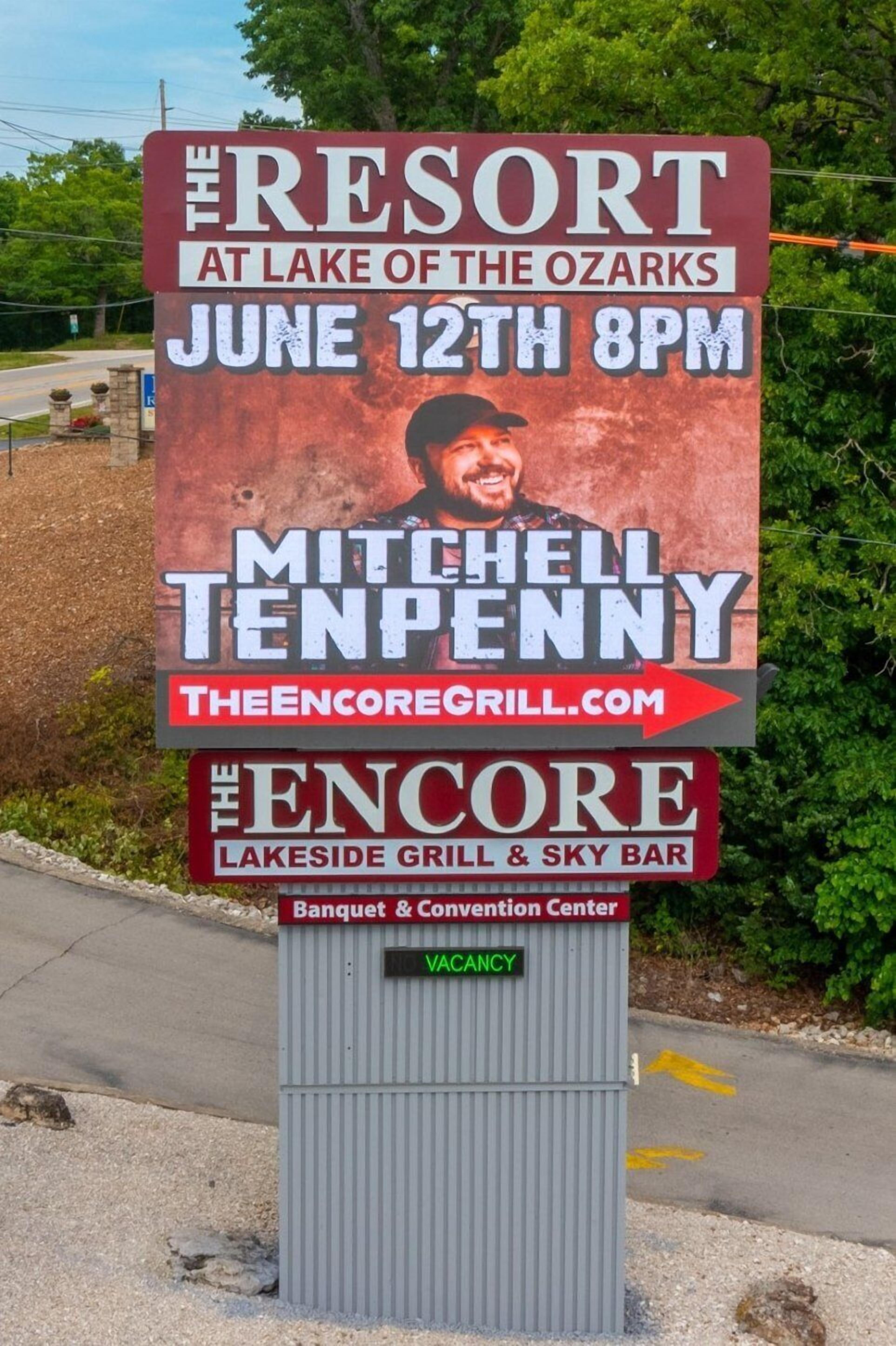 A sign for a resort at Lake of the Ozarks with a date and time for an event, a name, and a website.