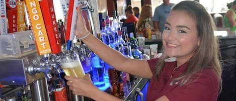 Un espace bar avec un barman préparant une boisson, une caisse enregistreuse, ainsi que diverses bouteilles et verres.