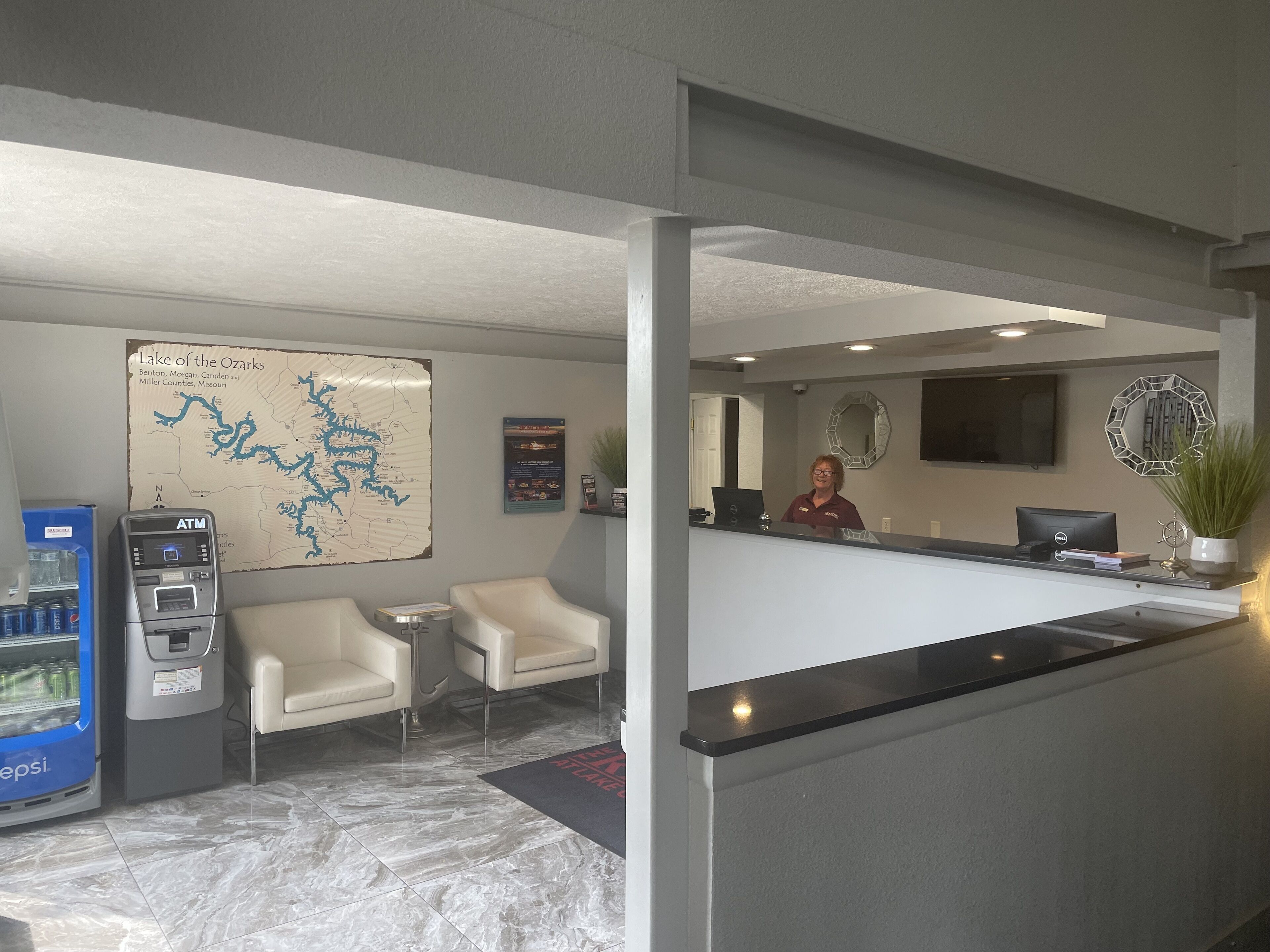 A hotel reception area with a map, a desk, chairs, an ATM, and a Pepsi refrigerator.