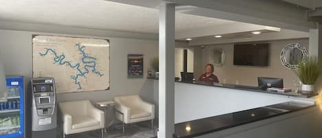 A hotel reception area with a map, a desk, chairs, an ATM, and a Pepsi refrigerator.