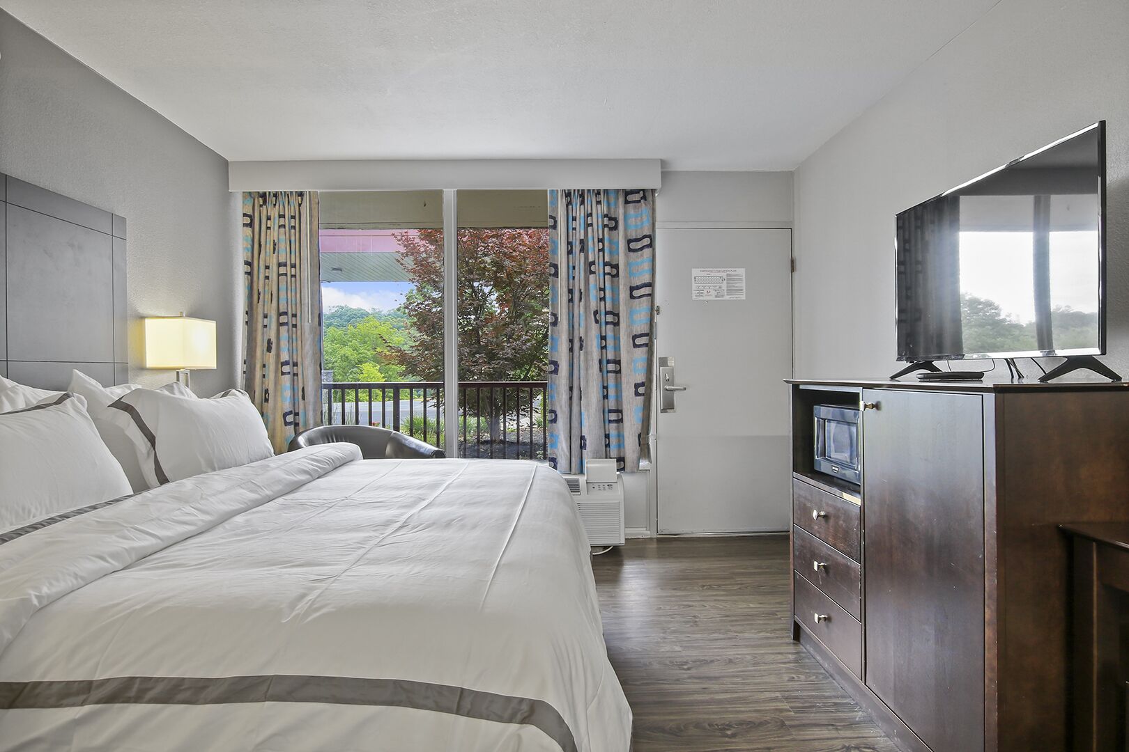 Une chambre d’hôtel avec un lit, une télévision, un bureau et une fenêtre avec des rideaux.