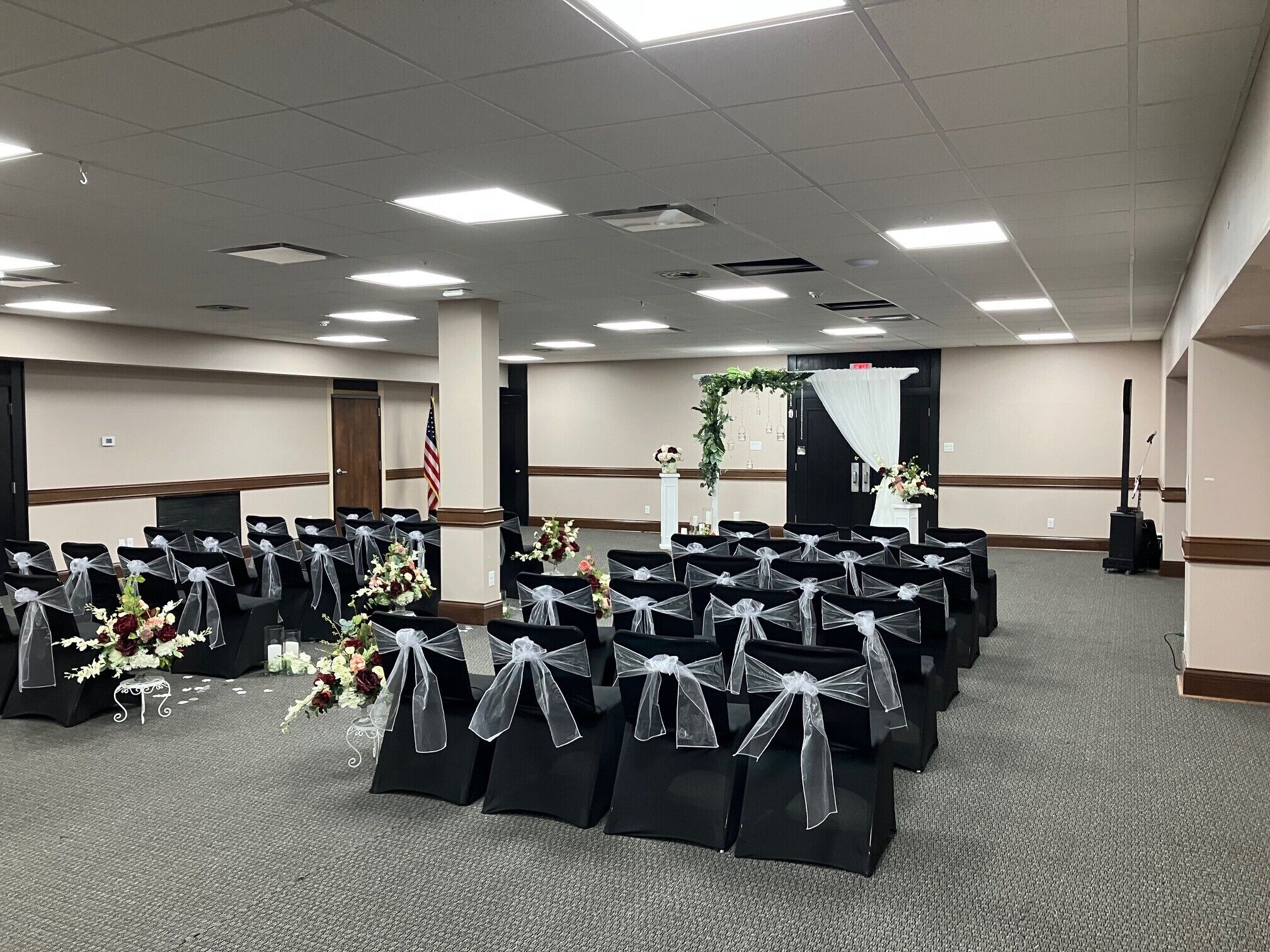 A conference room with rows of chairs, a stage with floral decorations, and an American flag.