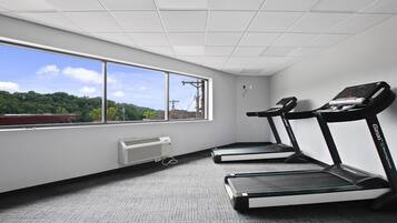 A gym with two treadmills, a window with a view of trees and buildings, and a ceiling with a grid pattern.