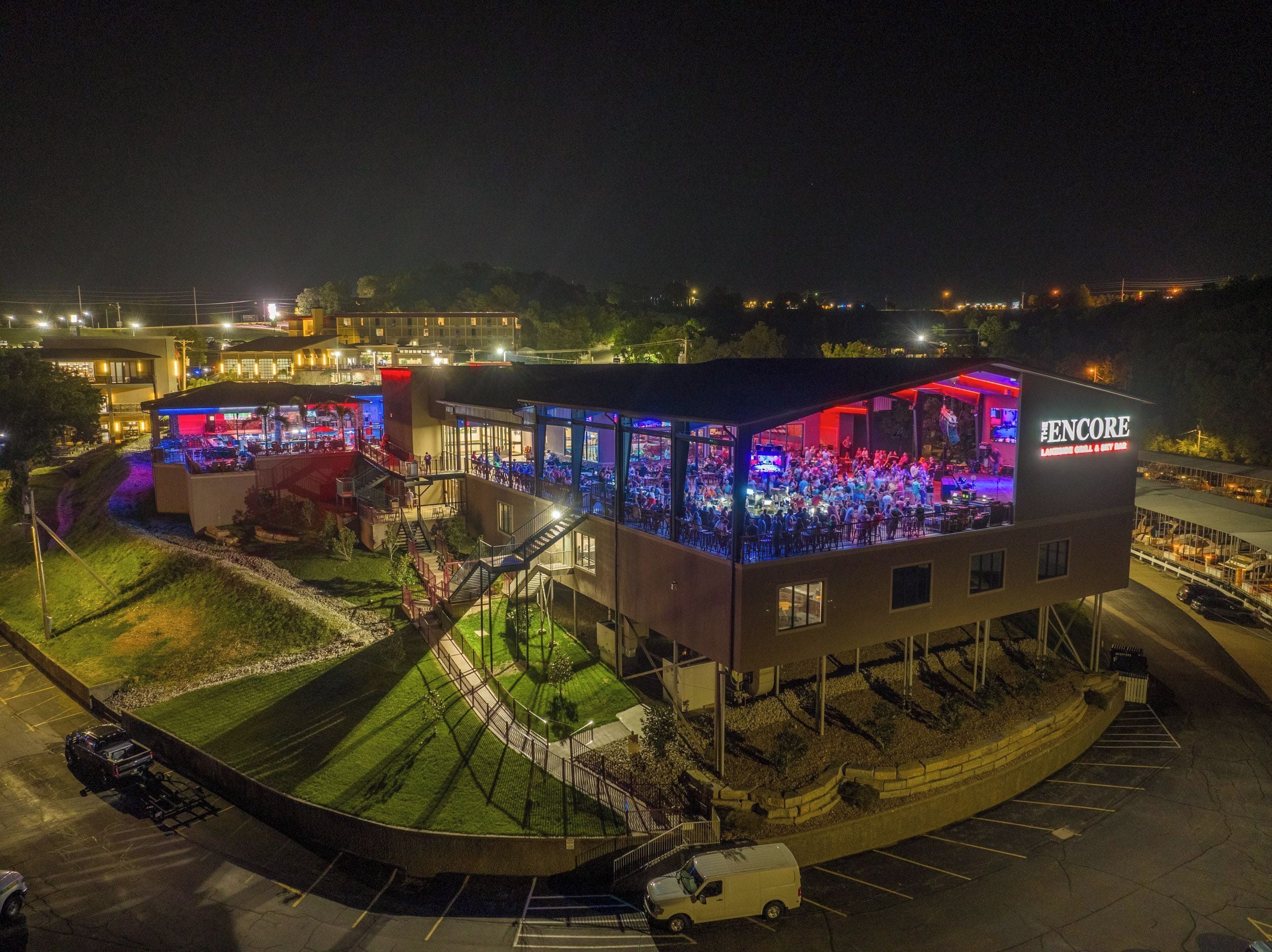 Un edificio de varios pisos con un amplio espacio de esparcimiento al aire libre y un escenario, iluminado por luces de colores.