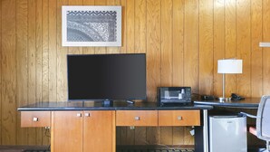 A hotel room with a wooden paneled wall, a flat-screen TV, a microwave, a desk, a chair, and a small refrigerator.