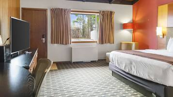 Une chambre d’hôtel avec un lit, un bureau avec une télévision, une fenêtre avec des rideaux, un radiateur et une lampe.