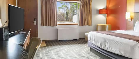 A hotel room with a bed, a desk with a TV, a window with curtains, a radiator, and a lamp.