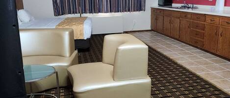 Habitación de hotel compacta con sofá, una mesita, televisión, kitchenette y alfombra estampada.