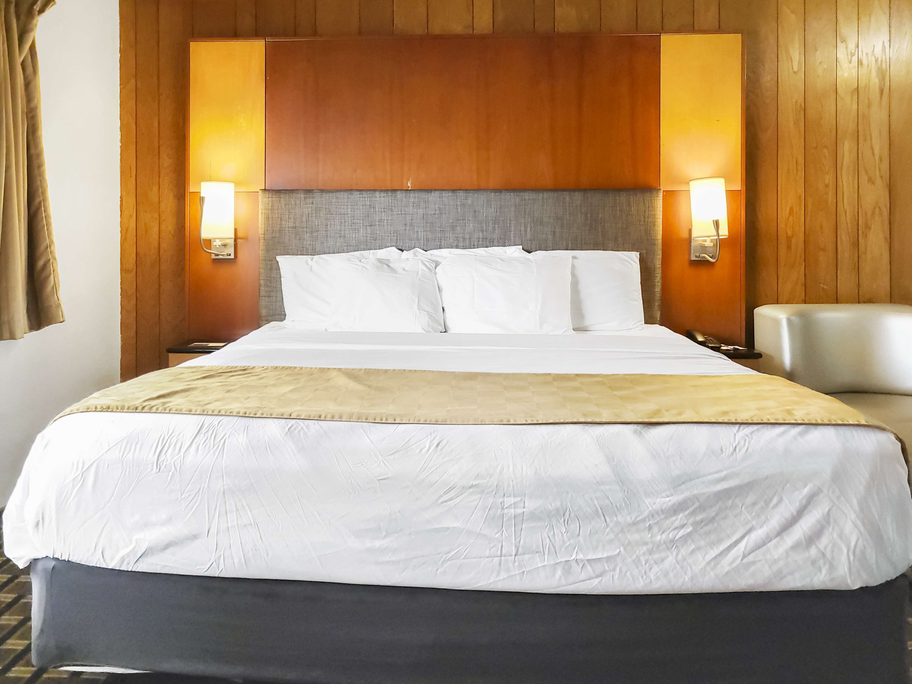 A hotel room with a large bed, two bedside lamps, a headboard, and a chair.