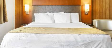 A hotel room with a large bed, two bedside lamps, a headboard, and a chair.