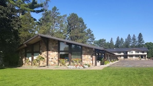 A two-story building with a stone facade and large windows, surrounded by a well-maintained lawn and trees.