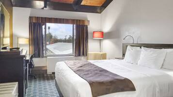 Ett hotellrum med en stor säng, ett skrivbord med en lampa, en stol och ett fönster med gardiner.